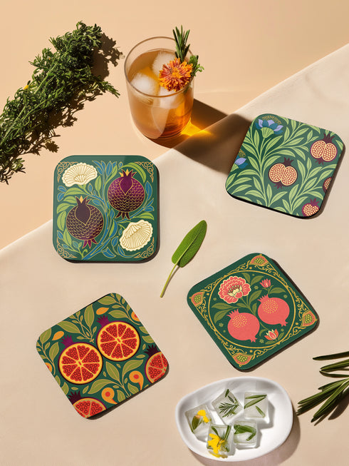 Set of four square drinking coasters featuring rich, dark green botanical illustration with highly detailed Pomegranate fruits and sliced cross-sections. The ornate pattern utilizes deep crimson, opulent gold, and ivory tones, strongly reflecting the stylized Art Nouveau period aesthetic and William Morris textile designs. Crafted from durable, resilient masonite hardboard, this luxury item features a protective high-gloss finish and a non-slip cork base.